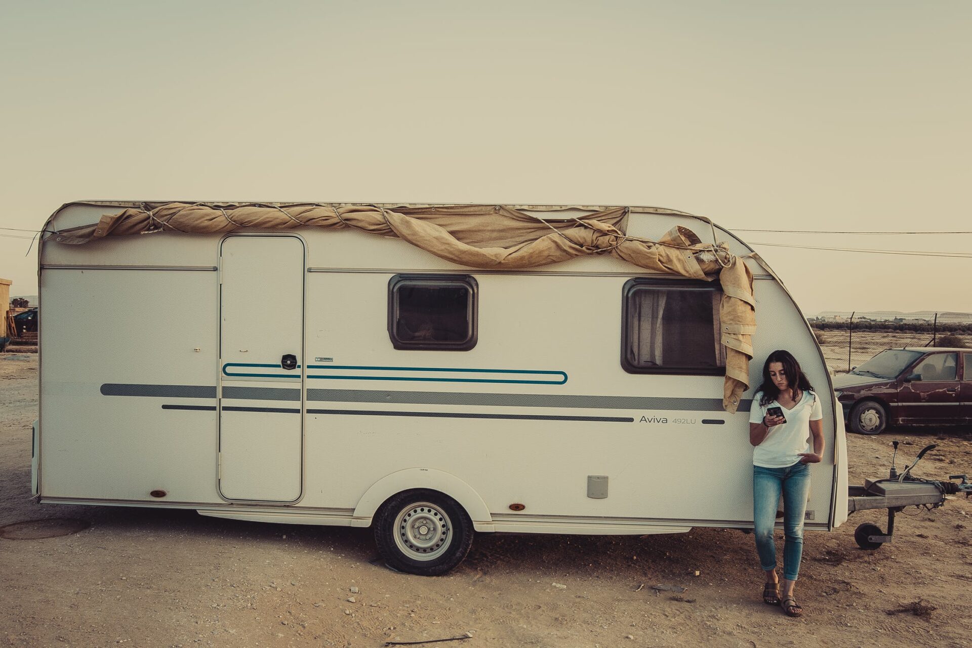 Young woman standing on a caravan window parked on a forest on a holiday adventure trip